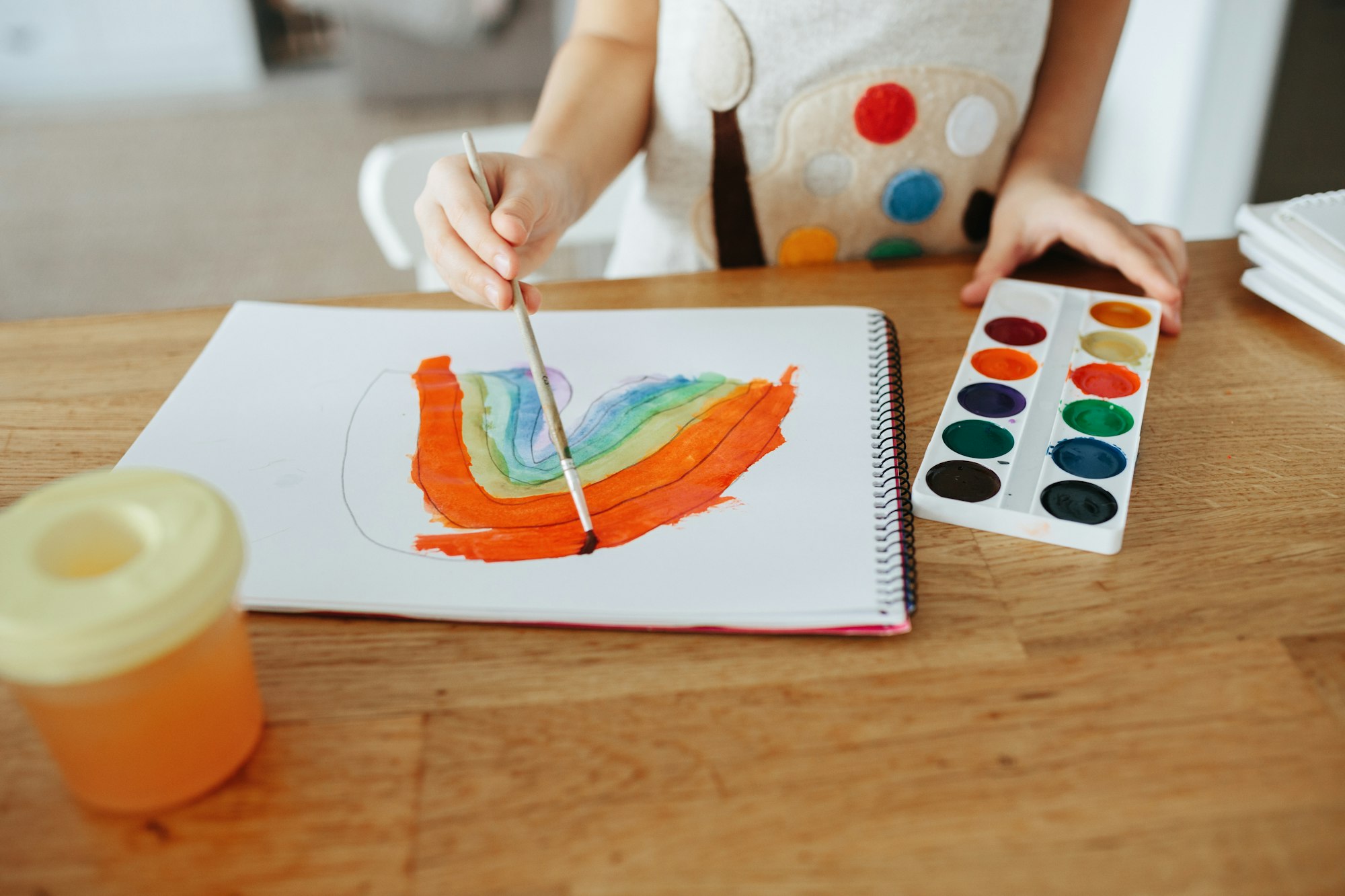 Kids painting watercolor rainbows at table at home