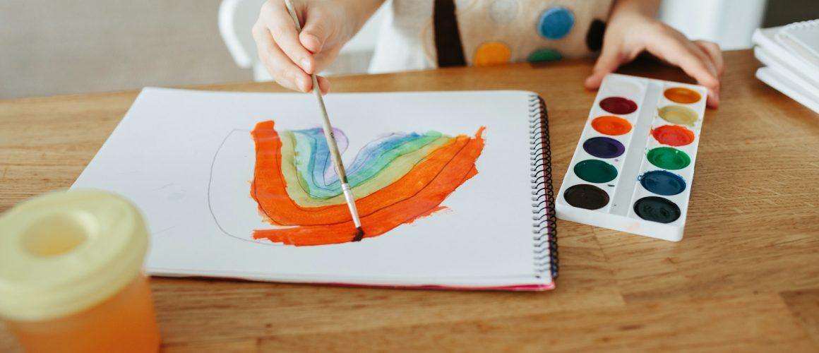 Kids painting watercolor rainbows at table at home