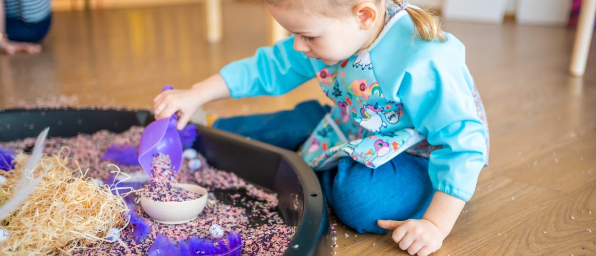 Little girl playing with sensory colorful rice. Sensory development and experiences, themed