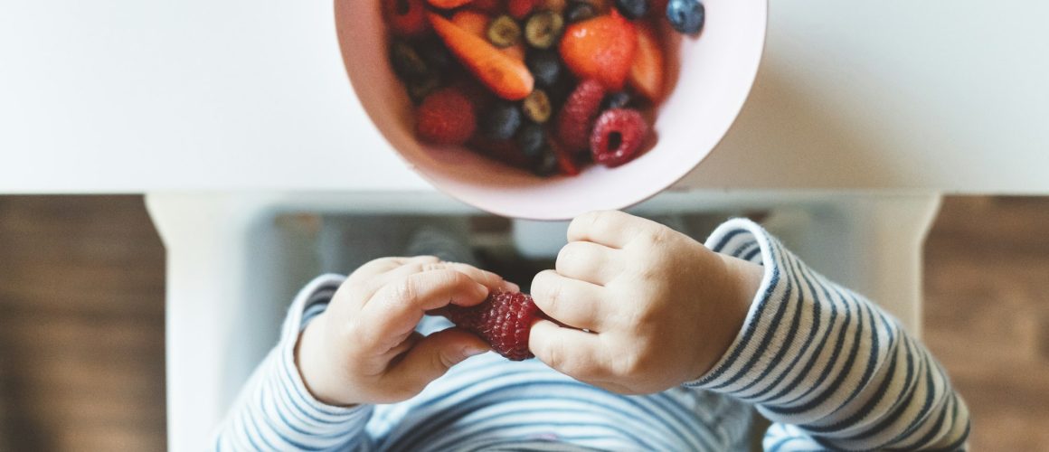 The baby is trying a new taste of solid food. Eating healthy food from the beginning is important. Y