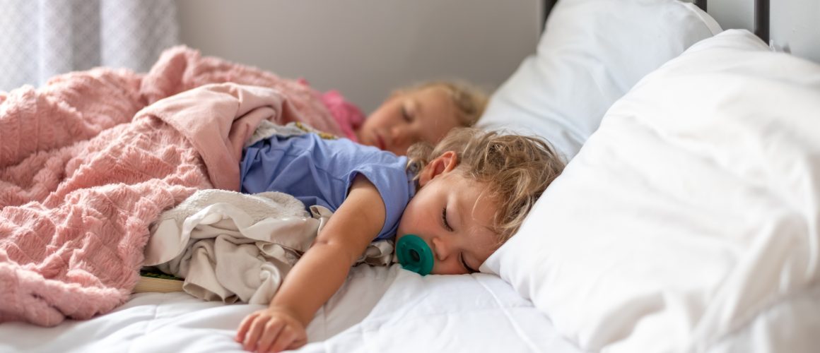 Two little girls napping on a big white bed